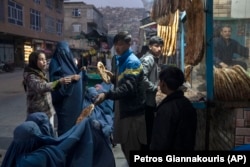 Egy férfi kenyeret oszt burkát viselő afgán nőknek egy pékség előtt Kabulban 2021. december 2-án