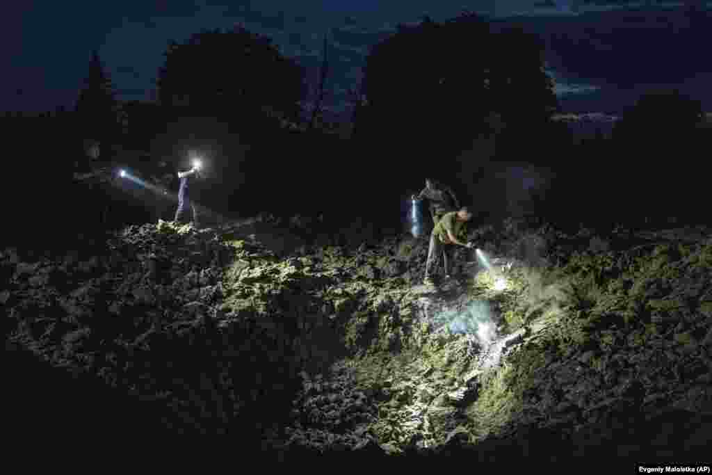 Upaljene baterijske lampe i potraga - ukrajinski policajci tragaju za ostacima rakete na mestu kratera ostalog nakon udara.