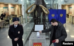 Un ofițer de poliție urmărește un bărbat care votează la o secție de votare de la Universitatea de Stat din Novosibirsk, Rusia, pe 17 martie.