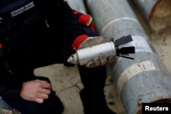 Ukrajinski vojni službenik Igor Ovcharruck drži deaktiviranu kasetnu bombu iz projektila MSLR, među izloženim komadima raketa koje je koristila ruska vojska, za koje je ukrajinski stručnjak za municiju rekao da nije eksplodirala pri udaru, u regiji Harkiv, Ukrajina, 21. oktobra 2022.