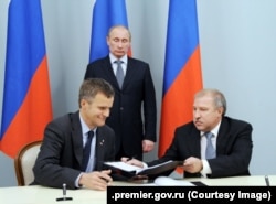 Președintele rus Vladimir Putin (în picioare) asistă la semnarea unui acord de cooperare strategică între Eduard Khudainatov (dreapta), pe atunci CEO al Rosneft, și Helge Lund, pe atunci CEO al Statoil ASA, la 5 mai 2012.