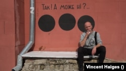 Hamlet Zinkivski sjedi ispred murala koji je napravio u Harkivu. Formulacija glasi: "Da! Ili možda ne?"