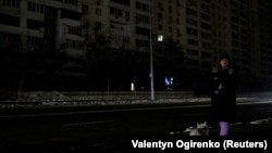 Жителка на Киев чака с кучето си на спирка на градския транспорт, потънала в мрак след руските обстрели в сряда.