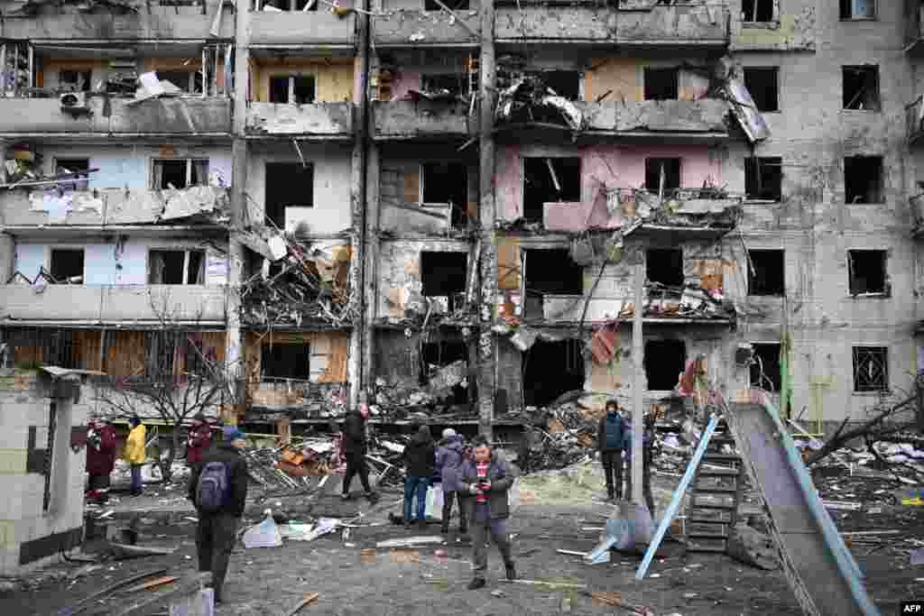 Njerëzit qëndrojnë jashtë një ndërtese banimi të shkatërruar në natën e dytë të sulmeve ruse, Kiev, 25 shkurt 2022. 