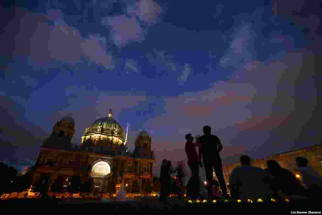 Și în Berlin, siturile istorice rămân în mare parte neiluminate după apusul soarelui. Oamenii se bucură de o seară de vară lângă catedrala centrală din Berlin. 