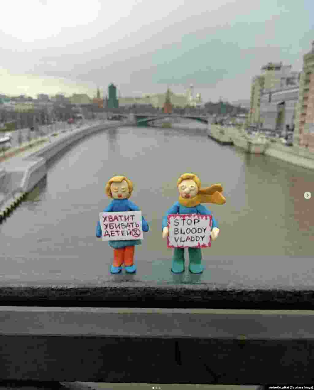 Figurine în fața Kremlinului, pe un pod deasupra râului Moscova. Semnul femeii spune: „Opriți uciderea copiilor.” Rușii care amplasează în public astfel de figurine de protest ar fi aproape sigur condamnați la ani grei de închisoare dacă ar fi prinși.