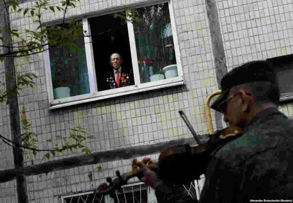 Një veteran 96-vjeçar i Luftës së Dytë Botërore shikon nga dritarja e apartamentit të tij, derisa një grup bën muzikë për nder të tij, gjatë festimeve të Ditës së Fitores, më 9 maj, në Donjeck të Ukrainës.