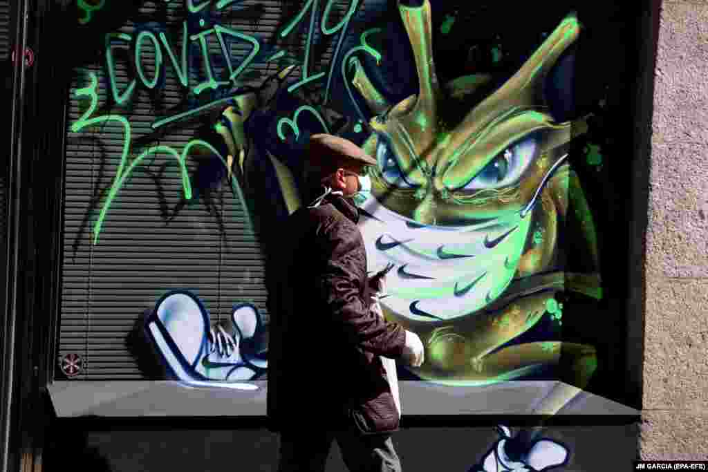 Një burrë në Salamanca të Spanjës kalon pranë një pikture murale për koronavirus.
