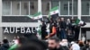 Mai mulți bărbați flutură steaguri siriene și germane în timpul unei manifestații de pe 8 decembrie, la Berlin, pentru a sărbători sfârșitul regimului lui Bashar al-Assad.