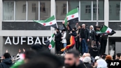 Mai mulți bărbați flutură steaguri siriene și germane în timpul unei manifestații de pe 8 decembrie, la Berlin, pentru a sărbători sfârșitul regimului lui Bashar al-Assad.