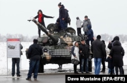 Localnici pozează pe un tanc T-72 al forțelor separatiste în timpul sărbătoririi Zilei Apărătorului Patriei la fostul aeroport din Luhansk, în februarie 2020.