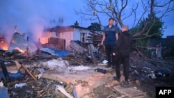 Localnici dintr-o suburbie a Harkovului pe ruinele caselor lovite de atacuri aeriene rusești, în zorii zilei de 21 mai, 2024. 