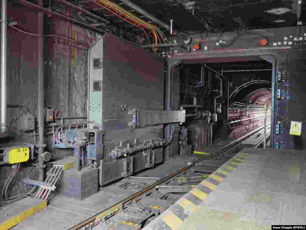 O ușă antiexplozie la stația de metrou Dejvicka din Praga, văzută în timp ce se apropie un tren. Cea mai mare parte a OSM a fost construită în timpul Războiului Rece, dar versiuni actualizate ale sistemului din era sovietică au fost încorporate în unele stații de metrou mai noi construite de Cehia independentă.