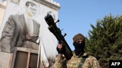 Un combatant antiguvernamental, pozând pe fundalul unui portret cu fața distrusă, al președintelui sirian, Bashar al-Assad, în orașul Hama capturat de forțele rebele, pe 6 decembrie 2024