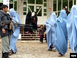 Un polițist afgan stă de pază în timp ce femeile îmbrăcate în burka pleacă după ce au participat la un seminar privind violența domestică în Herat. 24 noiembrie 2009