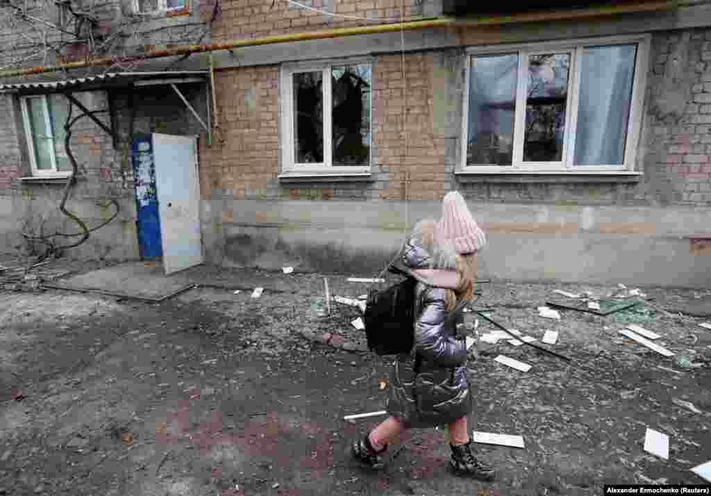 Një vajzë e vogël kalon pranë një ndërtese banimi, për të cilën vendasit thanë se ishte dëmtuar nga bombardimet e fundit, në qytetin Yasynuvata të kontrolluar nga separatistët në rajonin e Donjeckut, Ukrainë, 24 shkurt 2022.