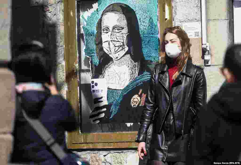 Një turiste në Barcelonë të Spanjës pozon para një pikture murale që tregon Mona Lizën me maskë.