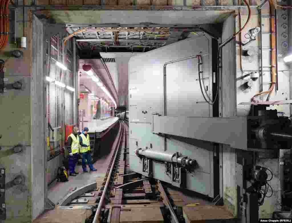 Inginerii privesc cum ușa antiexplozie este închisă deasupra șinelor de metrou.&nbsp; OSM a fost încorporat în rețeaua de metrou din Praga începând din 1974, când pericolul războiului nuclear era la ordinea zilei în Europa.